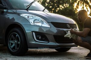 A man carefully cleans a car hood at sunset, focusing on details.